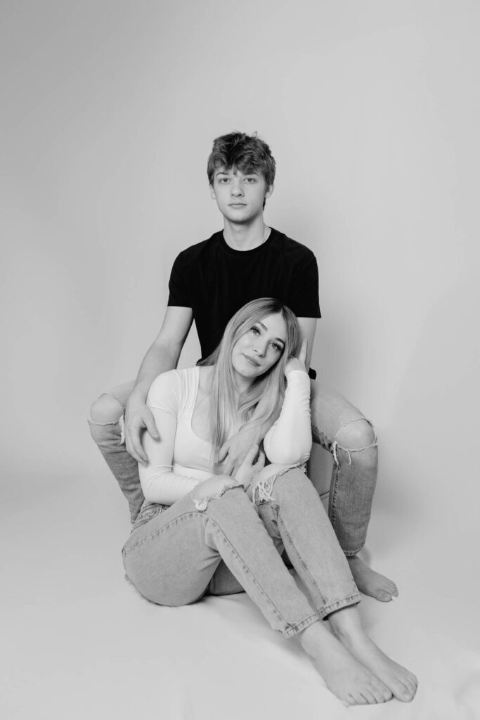 girl sitting on photoshoot backdrop floor while man sits behind her on hair and her face leaning into his arms