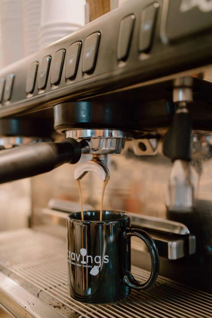 espresso being pored by a machine a black coffee mug