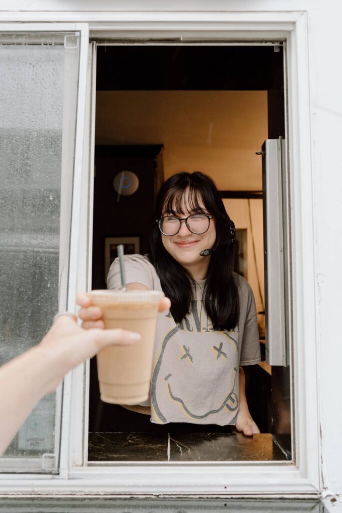 Barista holding coffee cup to customer throughwindow