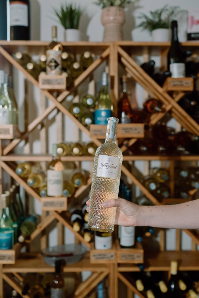 person holding a bottle of wine in  front of a rack full of other wines