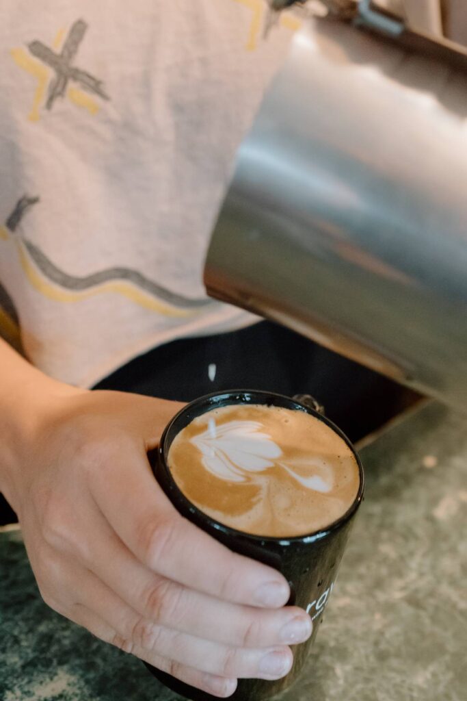 barista making coffee art in a black mug with milk