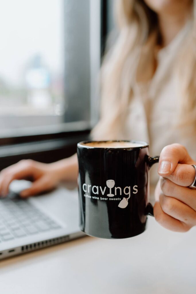 person working while also holding up their mug at a coffee shop for a photoshoot