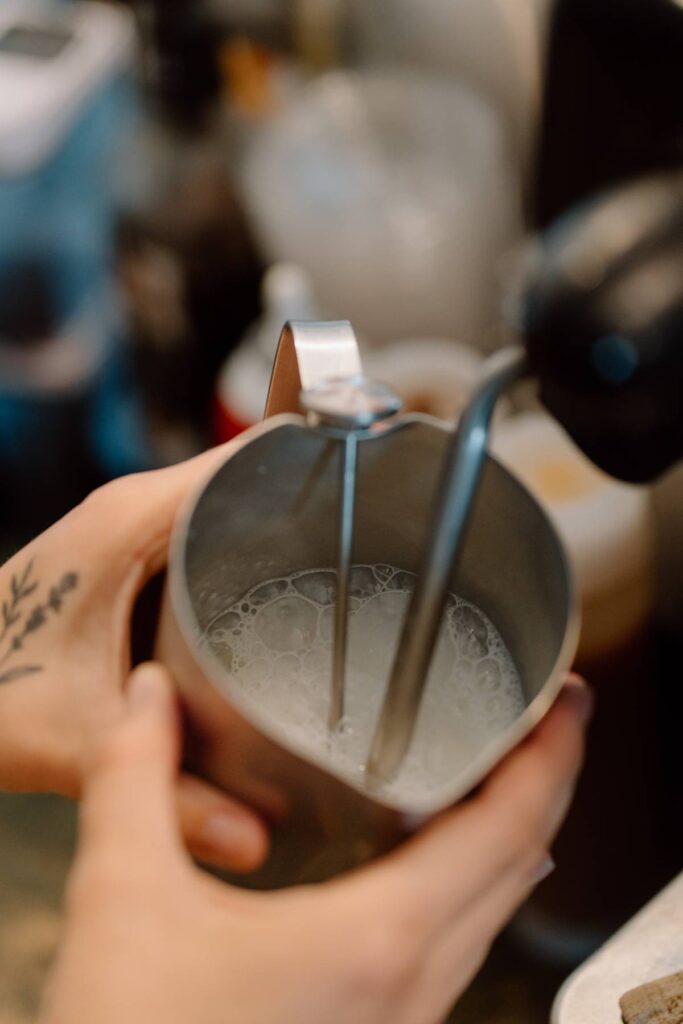 milk getting frothed in a metal mug by a coffee machine