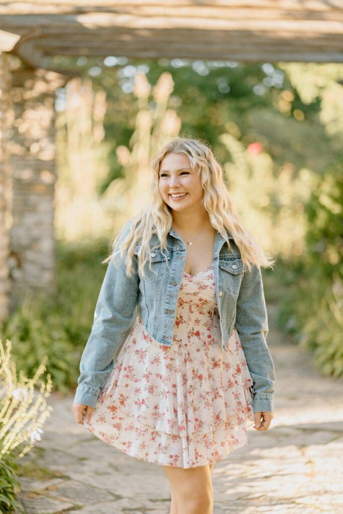 Full-body shot of Kalea in a flower garden with a soft breeze blowing her dress.
