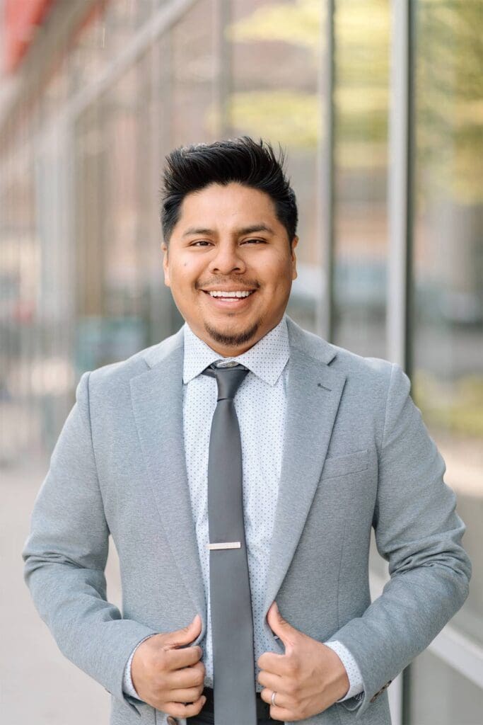 Professional Headshot of a man in a suit against windows in downtown milwaukee